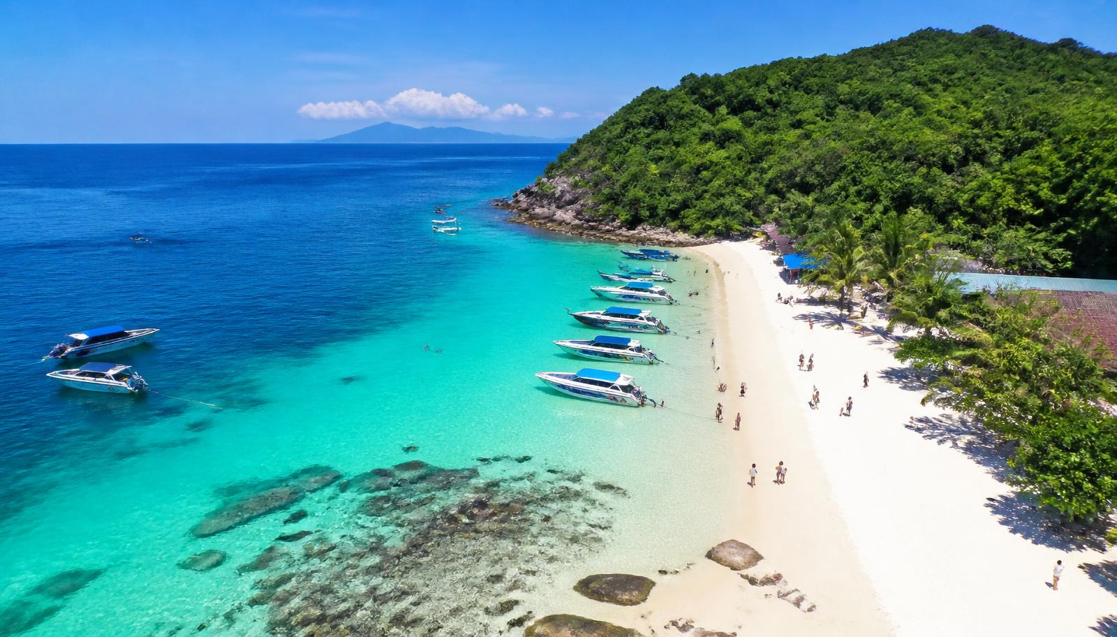 Clear turquoise water and white sand at a Koh Larn island beach near Pattaya with speedboats moored offshore